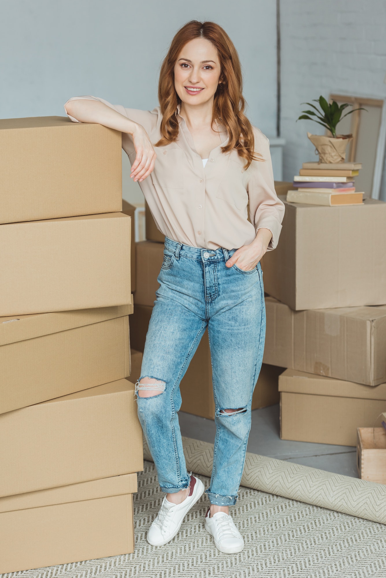 smiling woman leaning on pile of cardboard boxes at new home, relocation concept